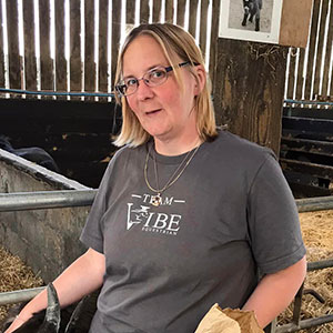 An image of Catherine, a woman with blonde hair and glasses she is standing in a barn infront of an animal pen.